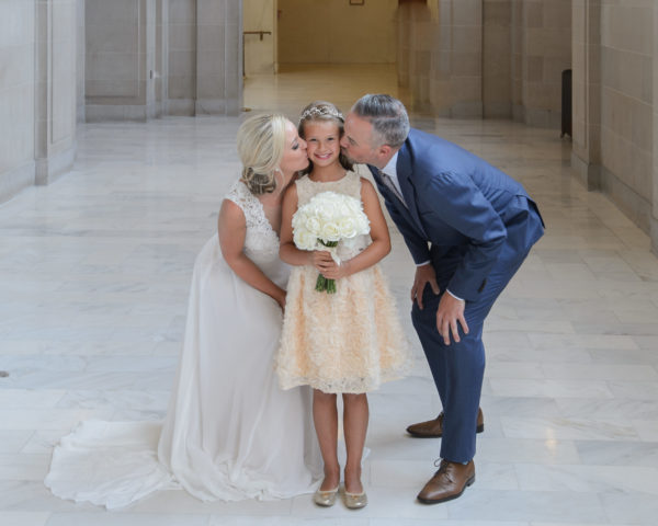 Bride and Groom kissing daughter