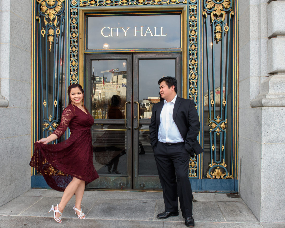 Bride and groom in front of city hall sign while twirling her dress. 