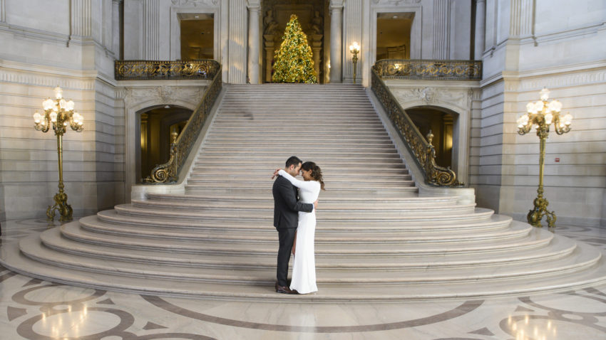 Bride and groom posing in front of The Grand Staircase at San Francisco city hall with the Christmas tree in the background