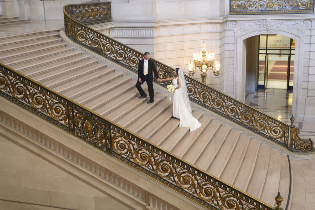 Groom helping bride up the Grand Staircase at SF City Hall
