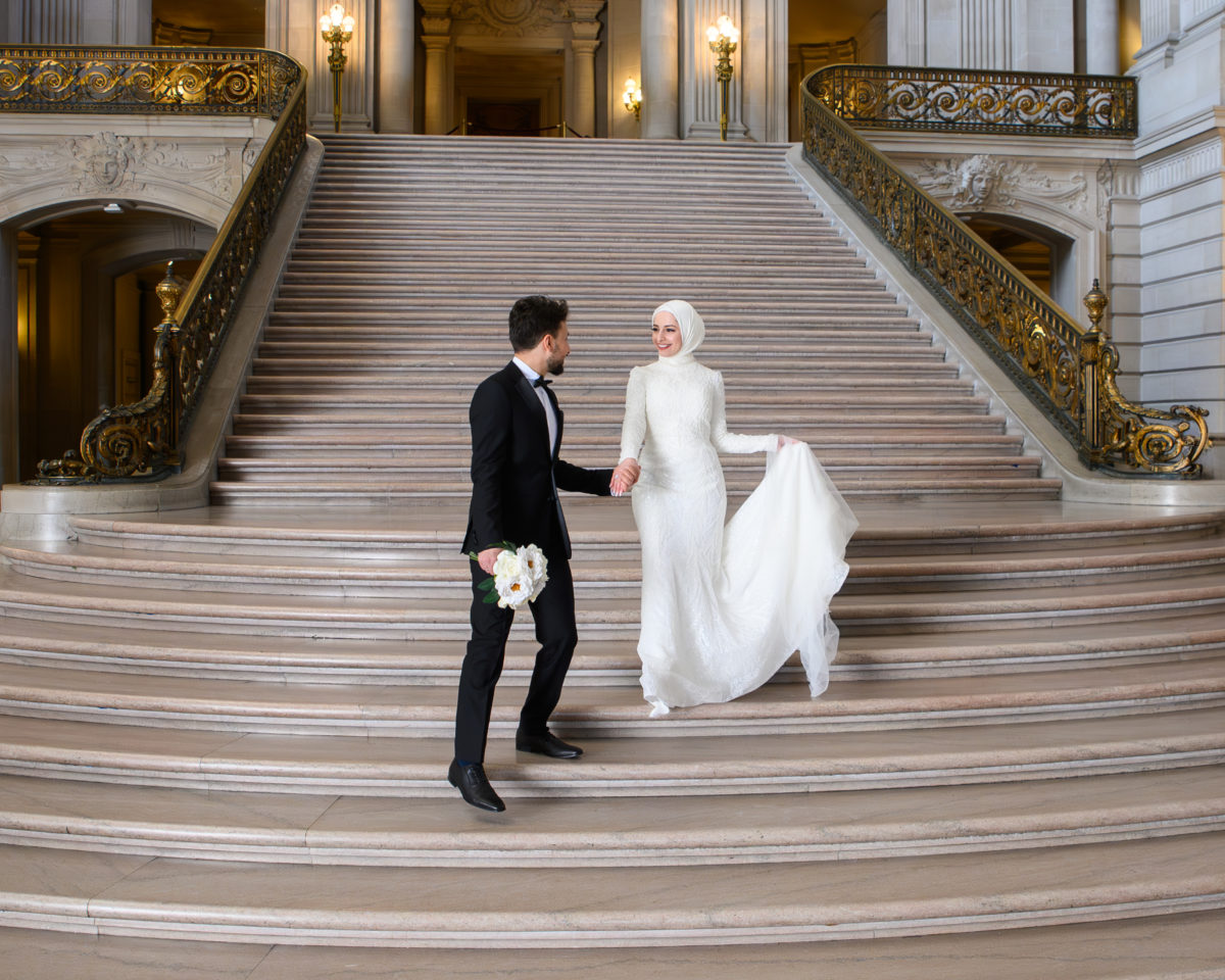 Groom leads bride down the grand Staircase at SF city hall