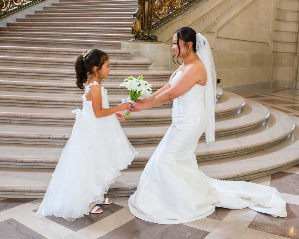Flower girl hands the bouquet to the bride at San Francisco city hall