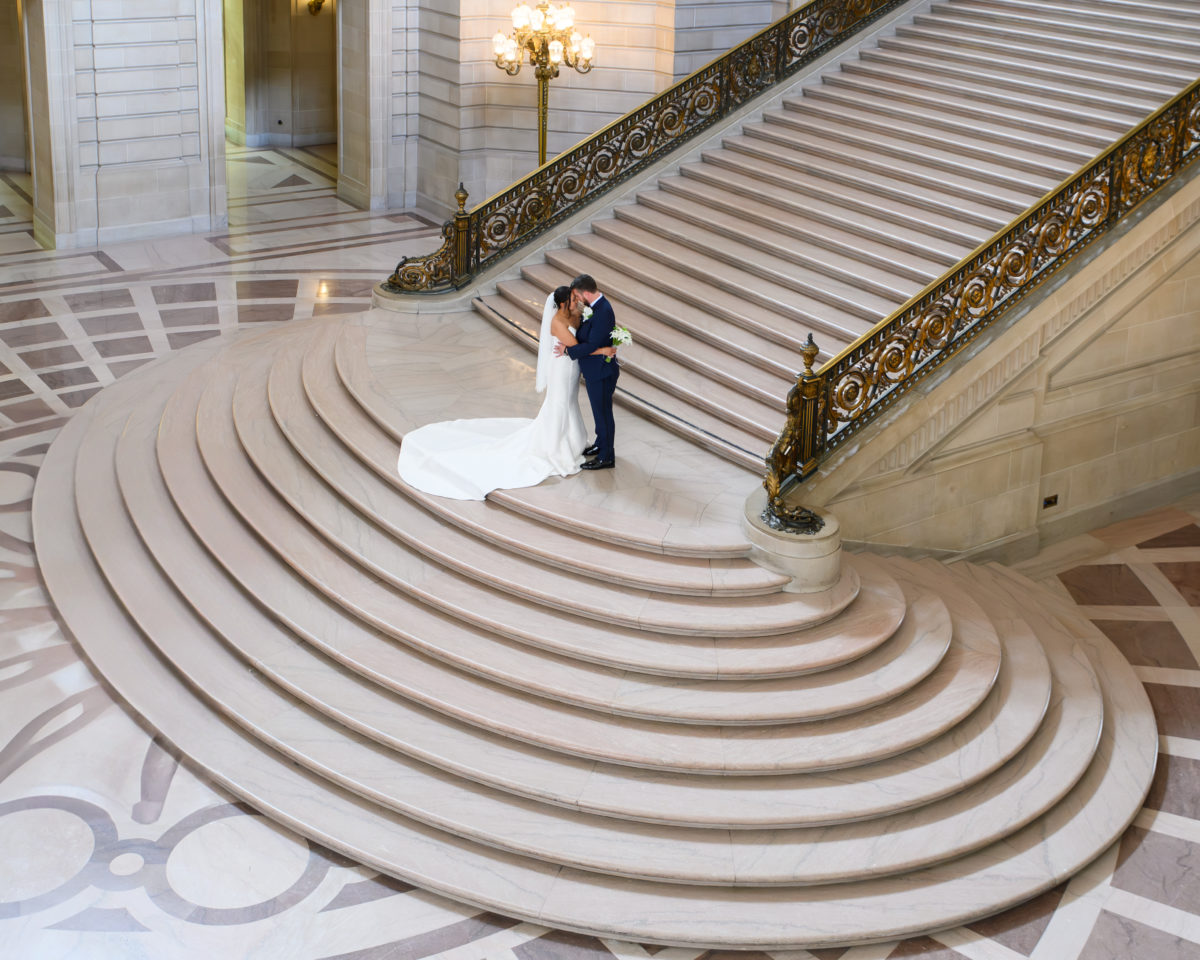 Wide angle view of bride and groom posing on the Grand Staircase at San Francisco city hall