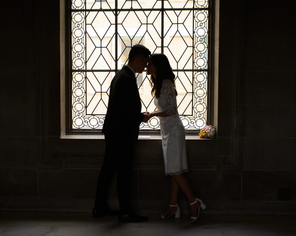 Bride and groom kissing in front of ornate window at San Francisco city hall
