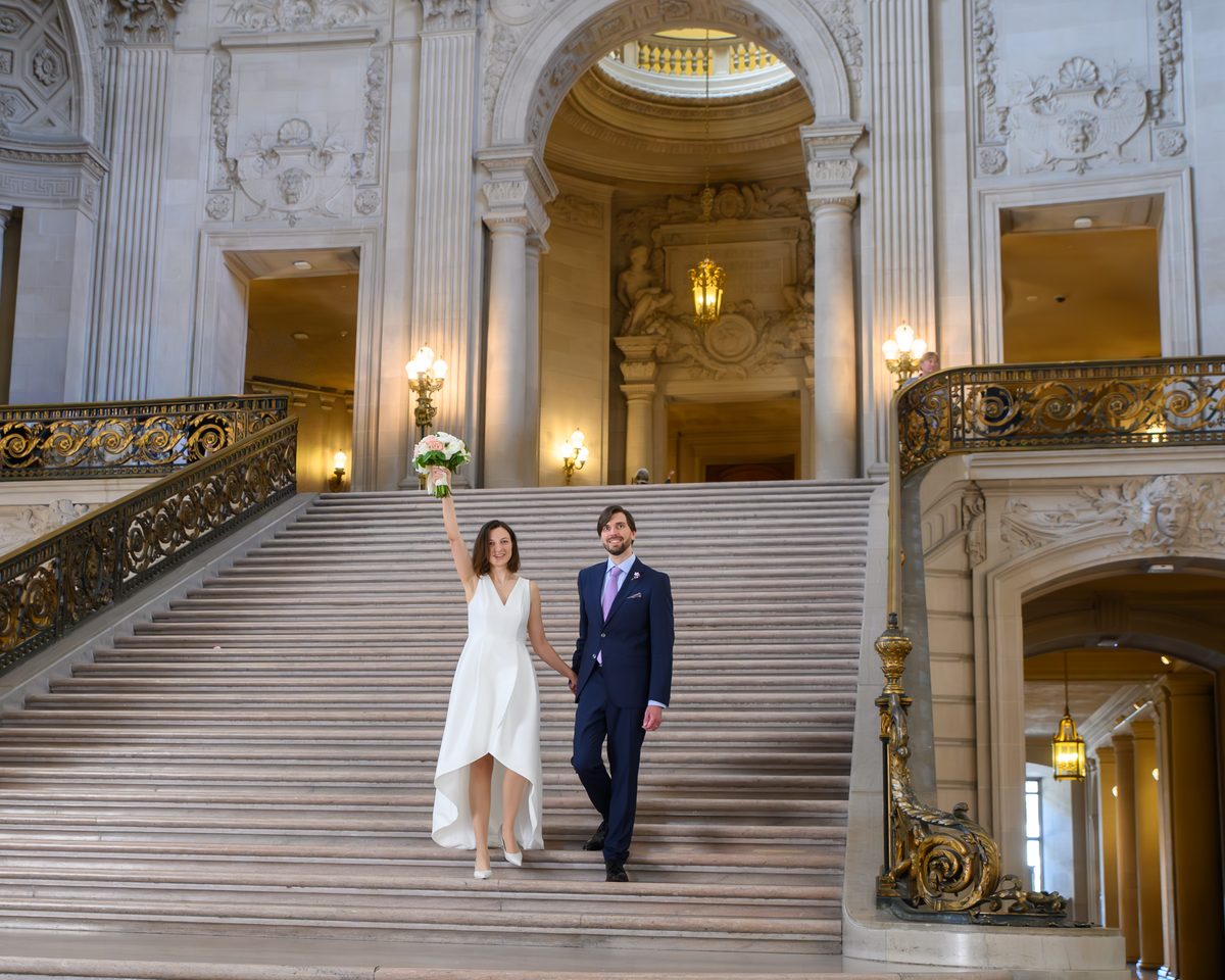 Newlyweds celebrating as they walk down the Grand Staircase at San Francisco city hall