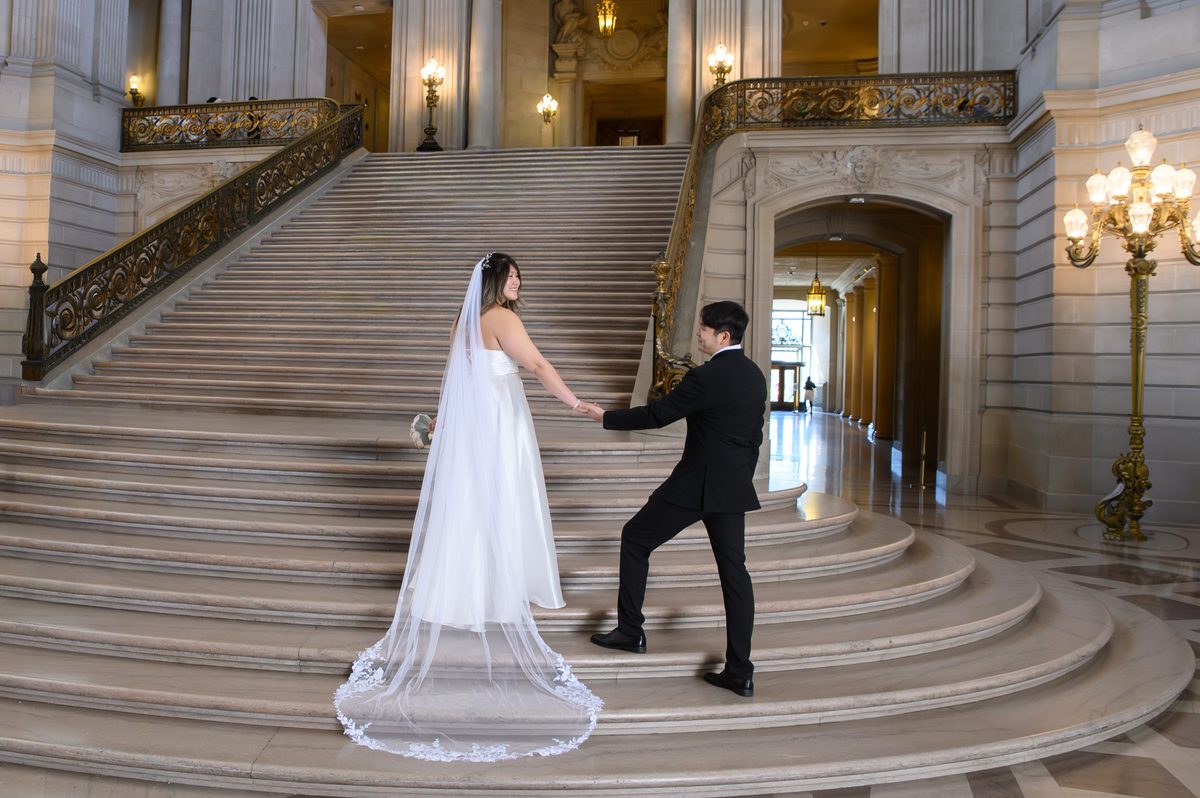 Groom hold the hand of his new bride on the Grand Staircase at San Francisco city hall