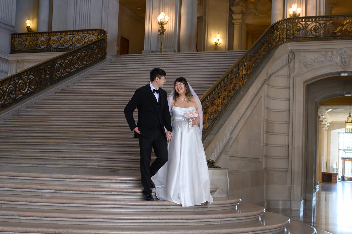 Happy newlyweds walking down the Grand Staircase just after their San Francisco city hall ceremony in the Rotunda